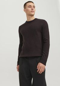 Maglione a maglia marrone scuro con scollatura rotonda e maniche lunghe. Presenta un orlo e polsini a coste, realizzato in un tessuto morbido e testurizzato.