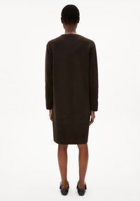 Braunes Langarmkleid, gerade geschnitten, knielang, aus strukturiertem Stoff; getragen mit schwarzen Absatzschuhen. Von hinten angezeigt.