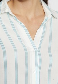 White button-up shirt with light blue vertical stripes. Features a classic collar and a soft cotton texture. Includes a front button placket.