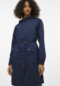Donkerblauwe, lichte regenjas met een capuchon, elastische manchetten, een trekkoord in de taille en twee lichaampockets, met gouden drukknoopsluitingen.