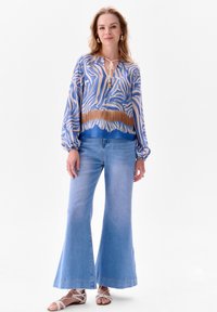 Blauw en beige zebra print blouse met lange mouwen, geknoopte halslijn, gedragen met lichtblauwe, uitlopende jeans en witte sandalen.