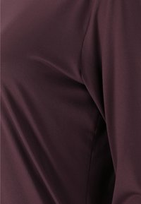 Burgunderfarbener Langarmtop aus glattem, dehnbarem Stoff, der eine schmeichelhafte Passform und minimalistische Nahtdetails für ein elegantes Erscheinungsbild bietet.