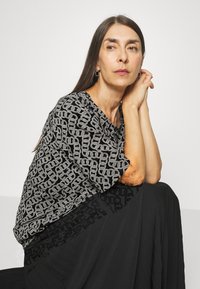 Top preto com padrão de corrente prateada, corte solto e decote barco, combinado com uma saia preta fluida. Texturas suaves e detalhes de design em camadas.