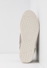 Chaussure basse avec une tige en suède gris et une semelle extérieure en caoutchouc texturée. Semelle blanche à motifs avec un détail circulaire au centre.