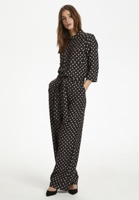 Schwarzer Jumpsuit aus Stoff mit weißem und pfirsichfarbenem Kreis-Muster, Taillenschleife, dreiviertellangen Ärmeln, weitem Bein und einem Kragen.