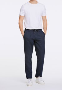 Navy modré kalhoty s elastickým pasem, bočními kapsami a volným střihem, doplněné o bílé tričko s krátkým rukávem a bílé tenisky.