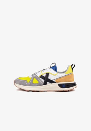 Colorful athletic shoe featuring mesh and suede materials, primarily yellow, gray, and white, with black and brown accents and a textured sole.