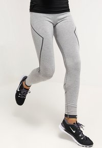 Szare legginsy sportowe z teksturowanym wzorem i czarnymi akcentami, zaprojektowane z myślą o ruchu, zestawione z czarno-białymi butami.