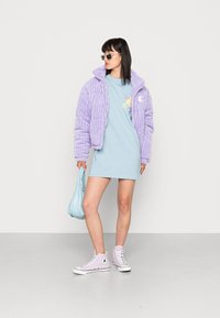 Casaco puffer de acolchoado em tons de lilás, com mangas curtas, combinado com um vestido t-shirt azul claro. Os acessórios incluem uma mala azul claro e sapatilhas cor-de-rosa.