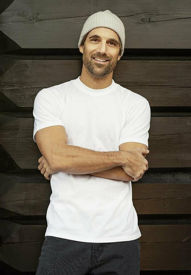 Hvit bomulls t-skjorte med korte ermer og rund hals, kombinert med mørk denim bukser. Modellen har en lys grå strikket lue.