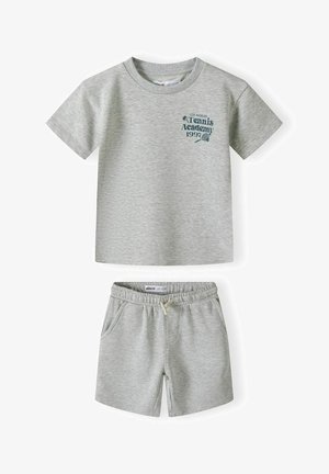 Siva pamučna majica kratkih rukava s natpisom "Tennis Academy 1997", u kombinaciji sa sivoj kratkim hlačama s elastičnom trakicom u struku i džepovima.