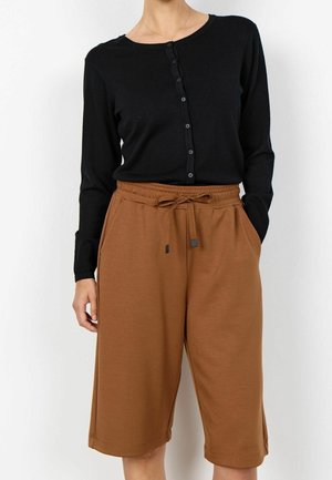 Personne portant un haut noir à manches longues boutonné et un short ample marron longueur genou avec une taille à cordon.