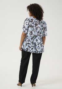 Blouse florale dans des nuances de bleu et noir, à manches courtes, en matière légère ; associée à un pantalon noir et des talons.