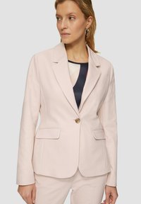 Lichtroze, op maat gemaakte blazer met gesneden revers, enkele knoopsluiting en twee voorzakken. Gladde textuur, geen zichtbare patronen of accenten.