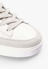 Hvide lædersneakers med grå ruskindsdetaljer, struktureret hvid gummisål og lysegrå snørebånd. Rund tå og syede detaljer.