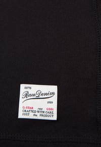 Czarna prążkowana tkanina z białą metką z napisem „Raw Denim” oraz tekstem zawierającym „G-STAR” i „crafted with care”. Widoczne zszyte brzegi.