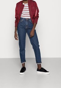 Röd bomberjacka med ribbade manschetter, randig t-shirt, högmidjade blå jeans och svarta sneakers. Anmärkningsvärda uppvikta manschetter på jeansen.