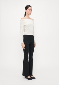Hvit off-shoulder langermet topp med ribbestruktur, kombinert med tettsittende svarte utvidede bukser og svarte flate sko.