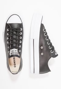 Fekete bőr Converse tornacipő fehér részletekkel, gumitalppal, fűzős kialakítással és jellegzetes logóval a nyelvén.