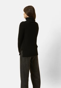 Schwarzer gestrickter Rollkragensweater mit lockerer Passform, geripptem Saum und seitlichen Schlitzen, kombiniert mit dunkelgrauen weiten Hosen.