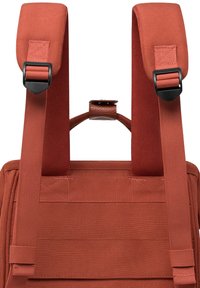 Red fabric backpack featuring padded shoulder straps with adjustable buckles, a top handle, and a textured surface.
