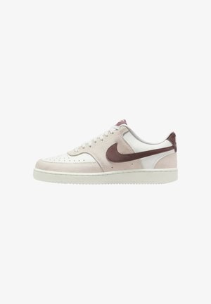 Basket basse en daim blanc et beige clair avec un swoosh Nike marron, des lacets blancs et une semelle blanche plate.