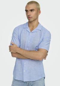 Lichtblauwtje kortärmige knoophemd met een soepele textuur, voorzien van een uitlopende kraag en een subtiel heatherpatroon, gedragen met jeans.