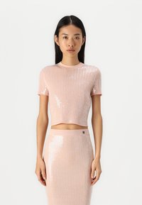 Svijetloružičasti rebrasti crop top s kratkim rukavima, ukrašen šljokicama i okruglim izrezom, u kombinaciji s odgovarajućom suknjom ukrašenom šljokicama.