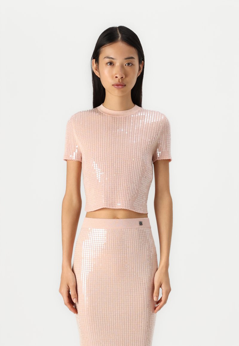 Svijetloružičasti rebrasti crop top s kratkim rukavima, ukrašen šljokicama i okruglim izrezom, u kombinaciji s odgovarajućom suknjom ukrašenom šljokicama.