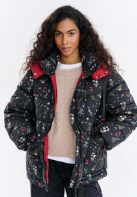 Czarna pikowana kurtka w kwiaty z czerwonym kołnierzem, zamkiem błyskawicznym z przodu i teksturowanym materiałem. Posiada kolorowe wzory kwiatowe na ciemnym tle.