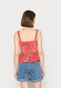 Top com estampado floral vermelho, com alças largas e costas quadradas, apresentando um design peplum, usado com calções de ganga azuis.