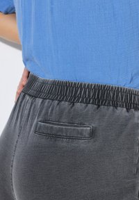 Šedé kalhoty s elastickým pasem a jednou zadní kapsou, s hladkým povrchem a jemným leskem, spárované se světle modrým topem.
