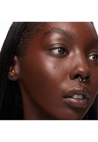 Primo piano di una persona dalla pelle scura con un piercing al setto nasale, pelle liscia e capelli neri lisci, con labbra dal tono naturale e occhi marroni.