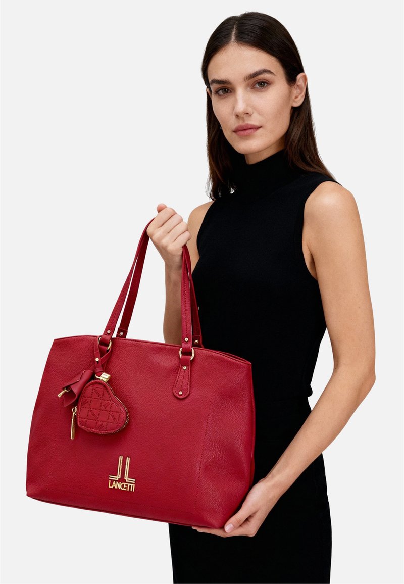 Borsa tote in pelle rossa con doppi manici, dotata di dettagli in oro. Include un piccolo charm a forma di cuore con motivo trapuntato e marchio.