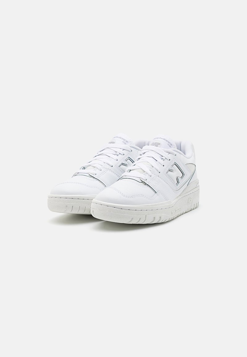 Paire de baskets basses blanches avec fermeture à lacets à l’avant et détails discrets du logo sur le côté, sur un fond clair uni.