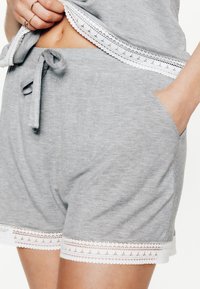Shorts en coton gris avec une bordure en dentelle à l'ourlet, taille à cordon de serrage et poches latérales. Le matériau a une texture douce et lisse.