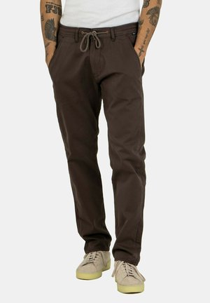 Braune Baumwollhosen mit einer lockeren Passform, Kordelzugbund und Seitentaschen, kombiniert mit hellen Sneakers.