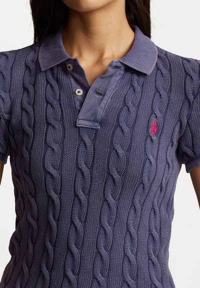 Polo en maille torsadée violette avec un col, une patte de boutonnage à trois boutons et un petit logo brodé sur le côté gauche.