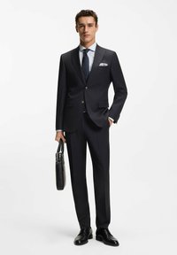 Garnitur w granatowy prążek o kroju dopasowanym, zestawiony z jasnoniebieską koszulą w paski i krawatem w kropki. Czarne skórzane buty i czarna teczka.