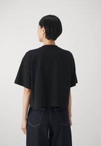 Zwart cropped t-shirt van katoen, met korte mouwen en een ronde halslijn, gecombineerd met donkere denim broek met contrasterende stiksels.