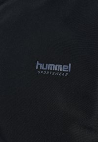 Czarny materiał sportowy z logo "hummel" w odcieniu szarości. Materiał wydaje się gładki z lekkim połyskiem, charakteryzuje się prostym i schludnym wzorem.