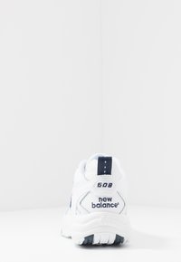 Sapata atlética branca com parte superior em couro, detalhes em azul-marinho, colarinho acolchoado e sola em borracha texturizada. Apresenta a marca "608" e "new balance".