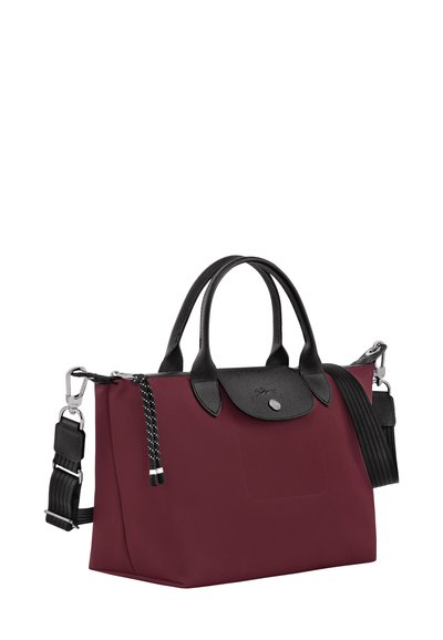 Red fabric handbag with black leather accents, double handles, detachable shoulder strap, and patterned tassels. Square shape with a button closure.