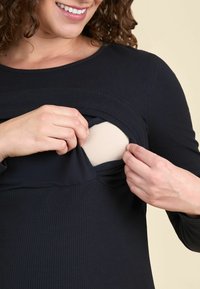 Top negru cu maneci lungi, cu o textura nervurată și un design stratificat, care arată un material bej dedesubt. Materialul pare elastic și se mulează pe corp.