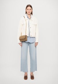 Veste en denim blanc sur une blouse à rayures bleu clair, associée à un jean large bleu clair et des chaussures à plateforme marron. Comprend un petit sac à main marron.