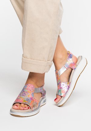 Feet wearing colorful floral open-toe sandals with thick white soles paired with beige rolled-up pants.