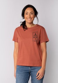 Es rustfarbenes Baumwoll-T-Shirt mit lockerer Passform, kurzen Ärmeln, Rundhalsausschnitt und einem schwarzen Justizwaage-Graphic auf der Vorderseite.