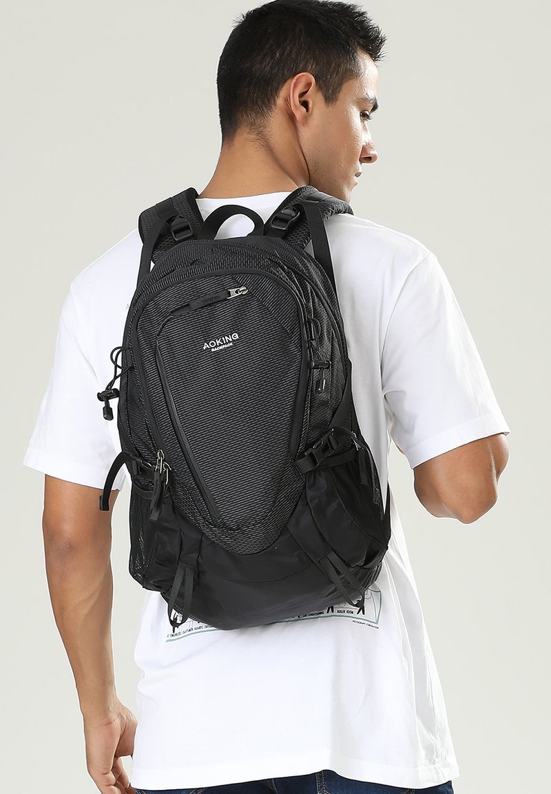 Zaino nero realizzato in materiale texturizzato, con una forma strutturata, scomparti con cerniera, spallacci regolabili e chiusure con coulisse.