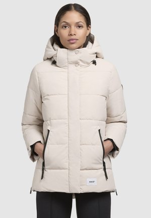 Giacca puffer beige con cappuccio foderato, tasche laterali con zip, chiusura a scatto e un motivo trapuntato testurizzato. Presenta una patch con logo vicino all'orlo.