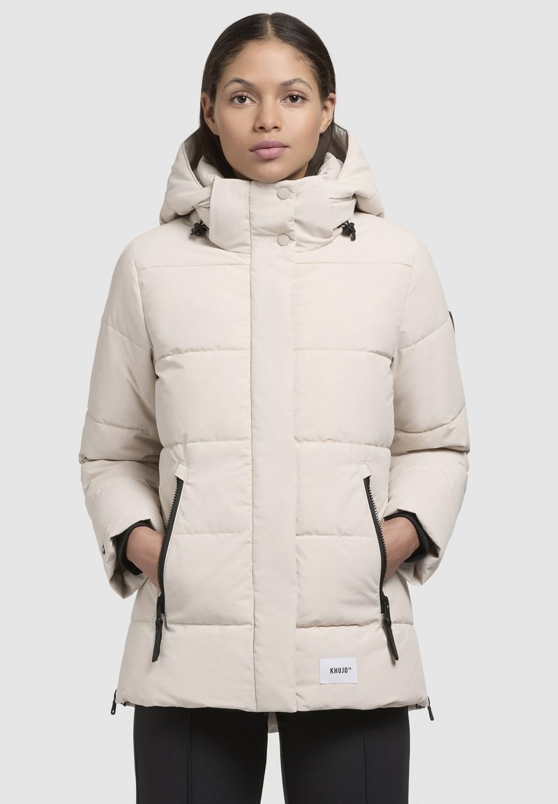 Beige Daunenjacke mit gefütterter Kapuze, seitlichen Reißverschlusstaschen, Druckknopfverschluss und einem strukturierten Steppmuster. Mit Logo-Patch nahe dem Saum.
